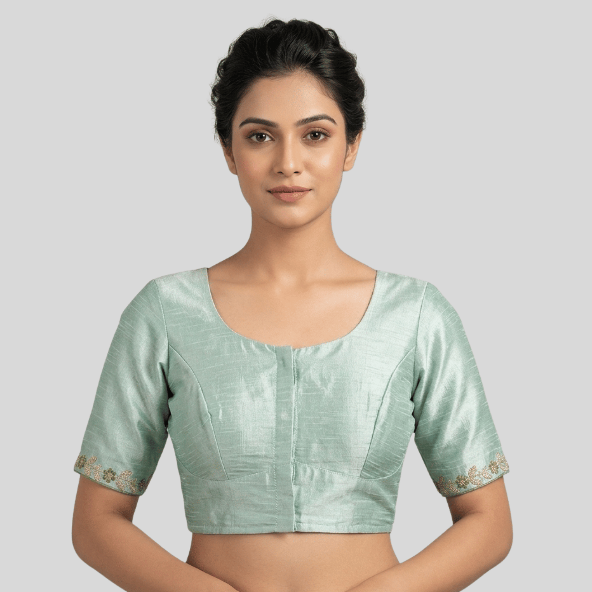 Woman wearing a light green blouse with floral embroidery on a plain background