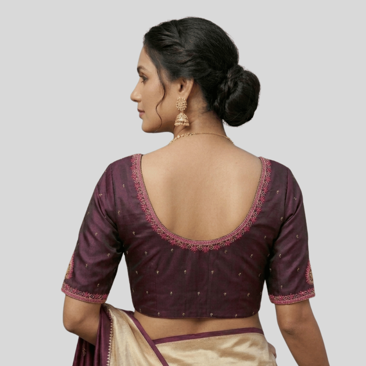 Woman wearing a traditional maroon blouse with gold embroidery on a plain background