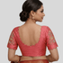 Woman wearing a pink blouse with intricate designs on a plain background